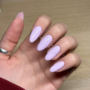 Hand with light purple nail polish on a wooden surface