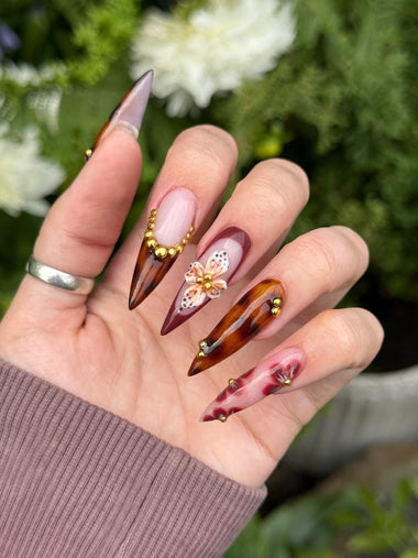 Hand with tortoiseshell and floral nail art against a blurred natural background