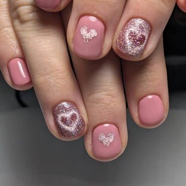 Close-up of a hand with pink / lilac  nails featuring heart designs and glitter