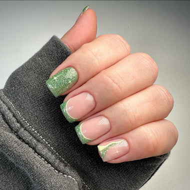 Hand with green glittery nail polish on a gray background
