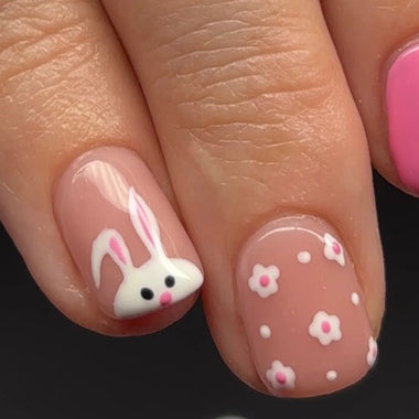 Close-up of a hand with pink nail polish and a decorative nail featuring a bunny design.