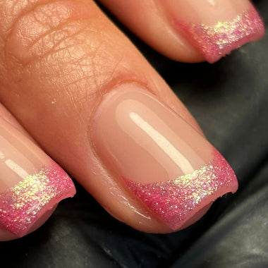 Close-up of a hand with pink and gold glittery nail polish on a dark background