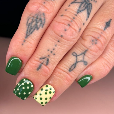 Close-up of hands with green nail polish and tattoos on a pink surface