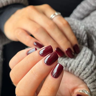 Close-up of hands with dark red nail polish wearing a gray sweater - halo gel nail polish shade toasty