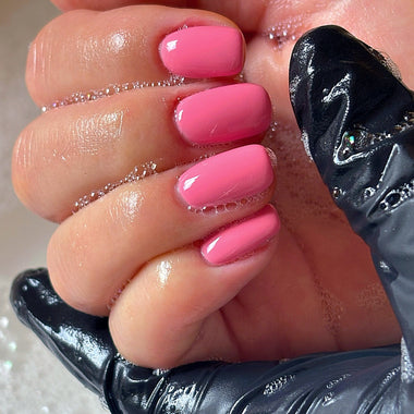 Close-up of a hand with pink nail polish wearing a black glove on a white background