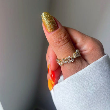 Hand with gold glittery nail polish wearing a silver ring on a neutral background