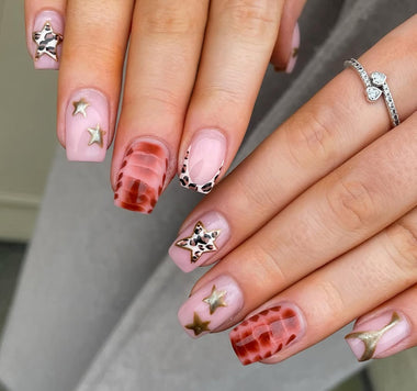 Close-up of hands with pink and gold star-shaped nail art on a neutral background