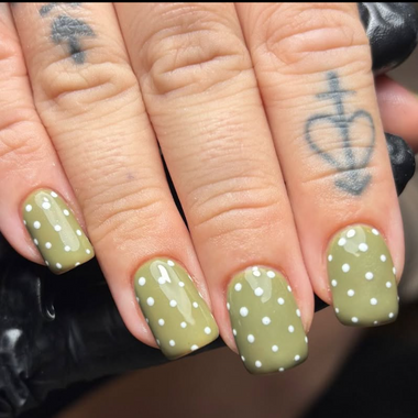Close-up of hands with green nail polish and white polka dots, featuring tattoos on the ring fingers.