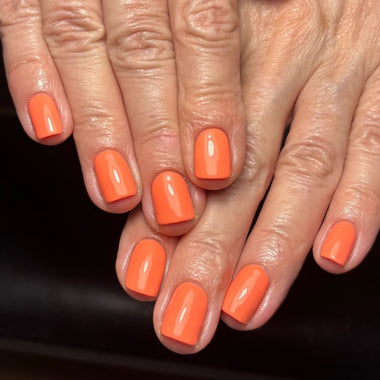 Close-up of hands with bright orange nail polish on a dark background