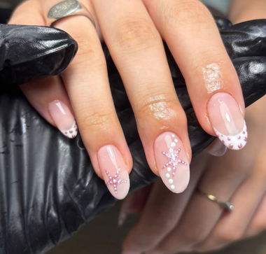 Close-up of hands with pink nail polish and glittery accents on a black surface.