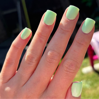 Hand with light green nail polish against a blurred outdoor background