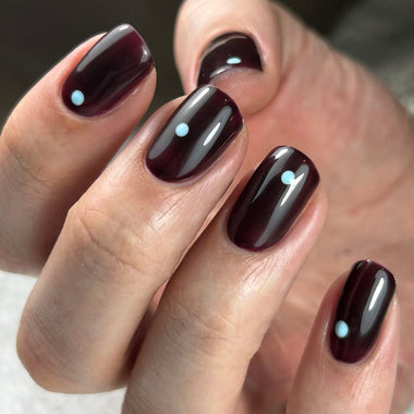 Close-up of a hand with dark red nail polish and small white dots on a blurred background
