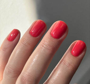 Close-up of a hand with bright red nail polish on a neutral background