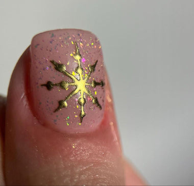 Nail with gold snowflake design on a light pink background