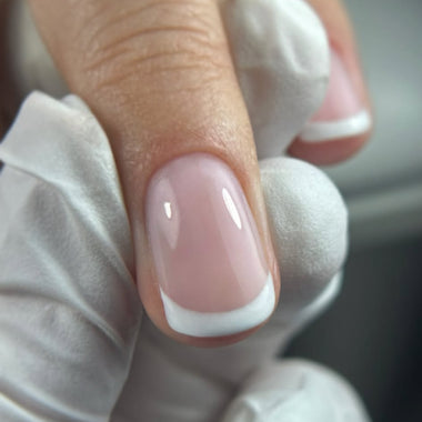 Close-up of a hand with a pink nail and white tip, wearing a white glove.