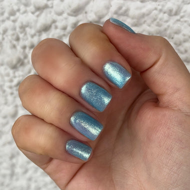 Hand with blue glittery nail polish on a textured white background