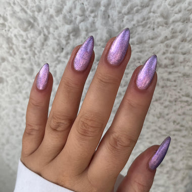 Hand with purple glittery nails against a neutral background