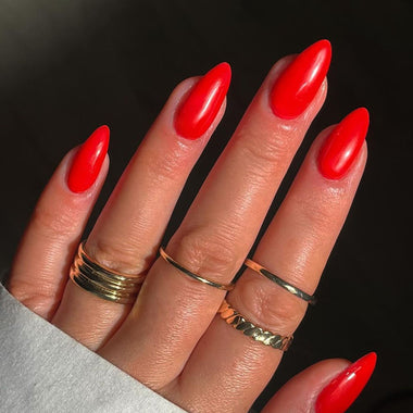 Hand with red nail polish and multiple gold rings on a dark background