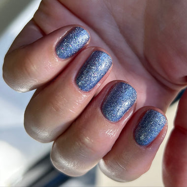Close-up of a hand with blue glittery nail polish on a blurred background