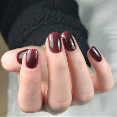 Close-up of a hand with dark red nail polish on a neutral background