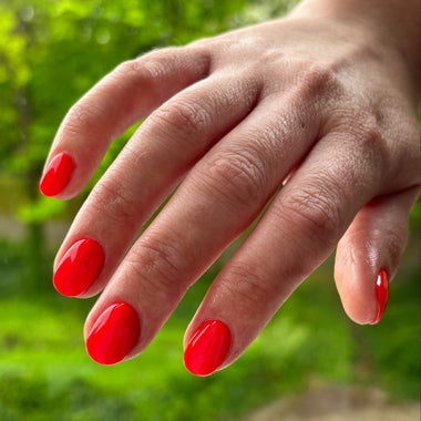 Hand with red nail polish against a green leafy background
