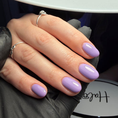 Hand with purple nail polish wearing a black glove, with a 'H' logo in the background.