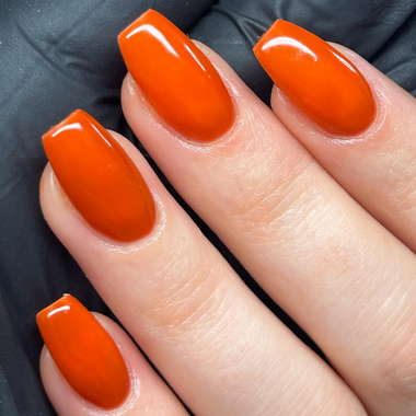 Close-up of a hand with bright orange nail polish on a dark background