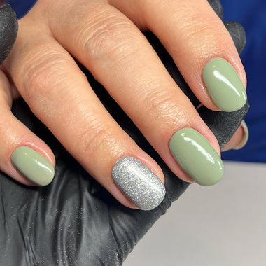 Hand with green and silver glittery nails wearing black gloves against a blue background