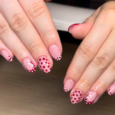 Close-up of hands with pink and red polka dot nail design on a neutral background HGP Burgundy