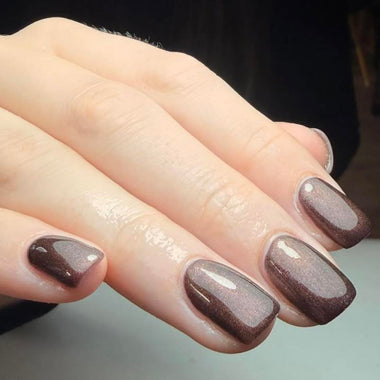 Close-up of a hand with brown nail polish on a neutral background