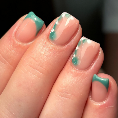 Close-up of a hand with teal and white nail polish on a blurred background