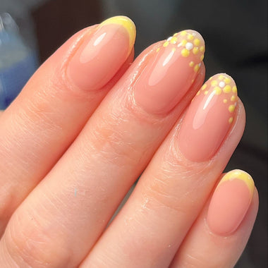 Hand with pink and yellow polka dot nail design on a blurred background