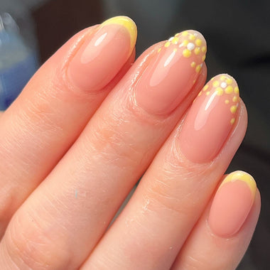 Close-up of a hand with pink nails and yellow polka dot designs.