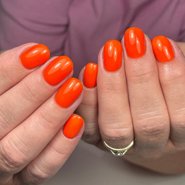 Close-up of hands with bright orange nail polish on a blurred background