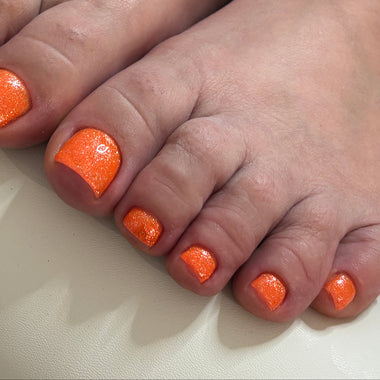 Close-up of feet with orange nail polish on a white surface