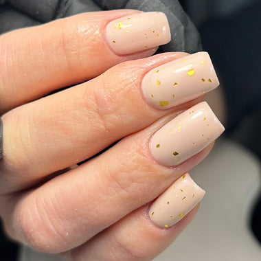 Close-up of a hand with beige nail polish and gold glitter dots on a blurred background