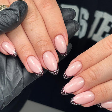 Close-up of hands with pink nail polish and black polka dots, wearing gray gloves.