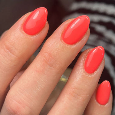 Close-up of a hand with bright coral nail polish on a blurred background