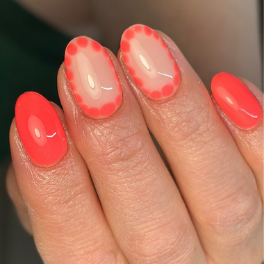 Close-up of a hand with bright coral nail polish on a blurred background