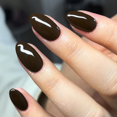 Close-up of a hand with dark brown nail polish on a blurred background