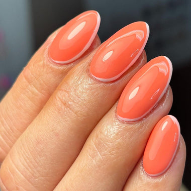 Close-up of a hand with orange-pink nail polish on a blurred background