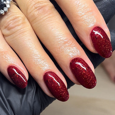 Close-up of hands with red glittery nail polish on a neutral background