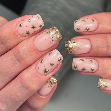 Close-up of hands with pink nail polish and gold glitter stars on a neutral background