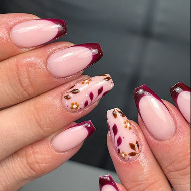 Close-up of a hand with pink and maroon nail design on a dark background