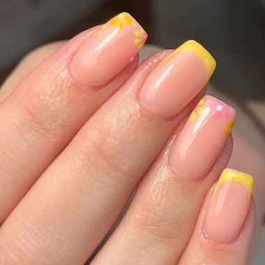 Close-up of a hand with pink and yellow nail polish on a blurred background