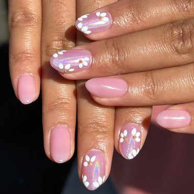 Close-up of hands with pink and white floral nail design on a dark background
