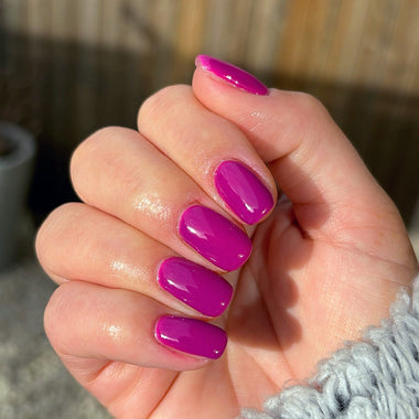 Hand with bright purple nail polish against a blurred outdoor background