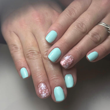 Close-up of hands with light blue nail polish and glittery accents on a neutral background
