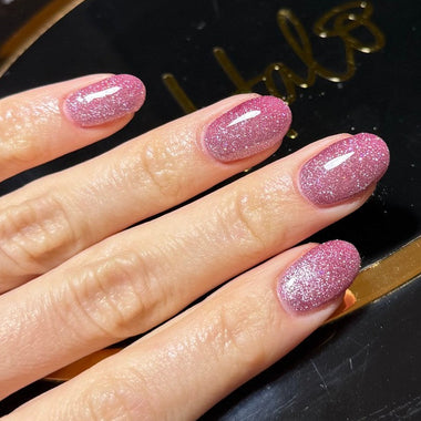 Hand with pink glittery nail polish on a black background
