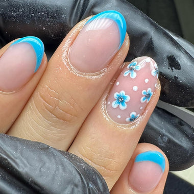 Nail art with blue flowers and white polka dots on a light pink background.